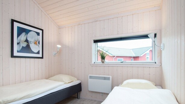 Una habitación con dos camas, un cuadro con flores, una ventana que da a un edificio rojo y un calentador fijado a la pared.