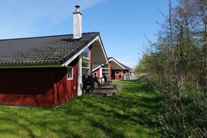 A red building with a sloped roof and a chimney, a deck with outdoor furniture, and a white fence. - Wunderschönes Ostsee-Cottage für 6 Personen (Großenbrode)