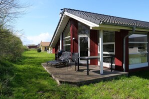 A bungalow with a covered porch, outdoor seating, and a view of the surrounding area. - Wunderschönes Ostsee-Cottage für 6 Personen (Großenbrode)