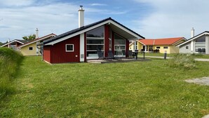 Moderni rakennus, jonka ulkoseinät ovat punaiset, siinä on suuret ikkunat ja katettu ulkoalue, jossa on istumapaikkoja.