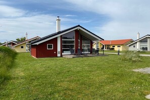 A modern building with a red exterior, large windows, and a covered outdoor seating area. - Nordische Familienentflucht mit Sauna (Großenbrode)