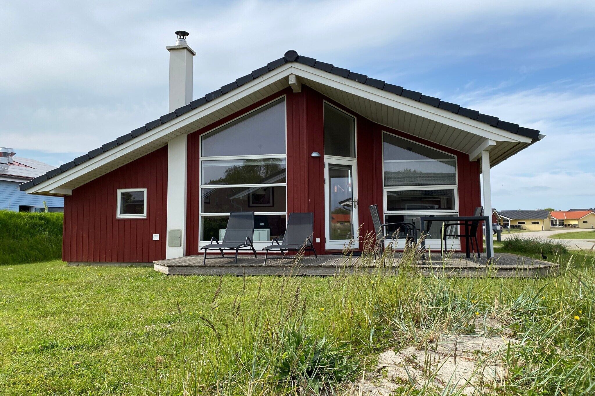 A modern house with a red exterior, large windows, and a covered porch with chairs.