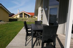 An outdoor patio with a table and chairs, a wooden deck, and a building with a number sign. - Luxuriöse Lodge an der Küste mit Sauna (Großenbrode)