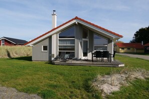 Een laag gebouw met een rood dak, een grote schuifpui en een klein terras met tuinmeubilair.