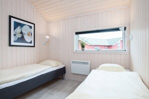 A room with two beds, a framed picture of flowers, a window with a view of a red building, and a wall-mounted heater. - Nordic Spa Lodge für 6 Personen (Großenbrode)