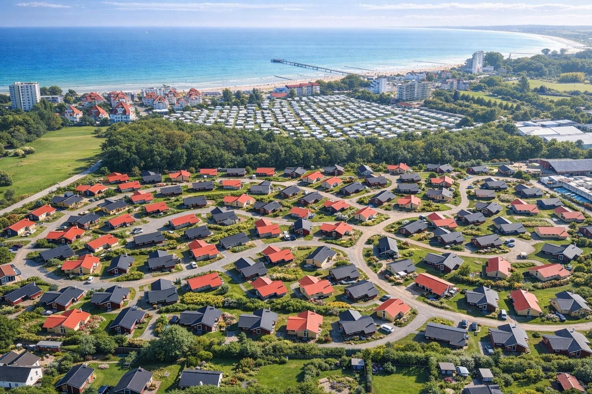 Un quartier résidentiel où les maisons sont disposées en cercle, avec une plage et une jetée en arrière-plan.