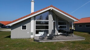 Ein modernes Haus mit geneigtem Dach, großen Fenstern und einer Terrasse mit Gartenmöbeln.