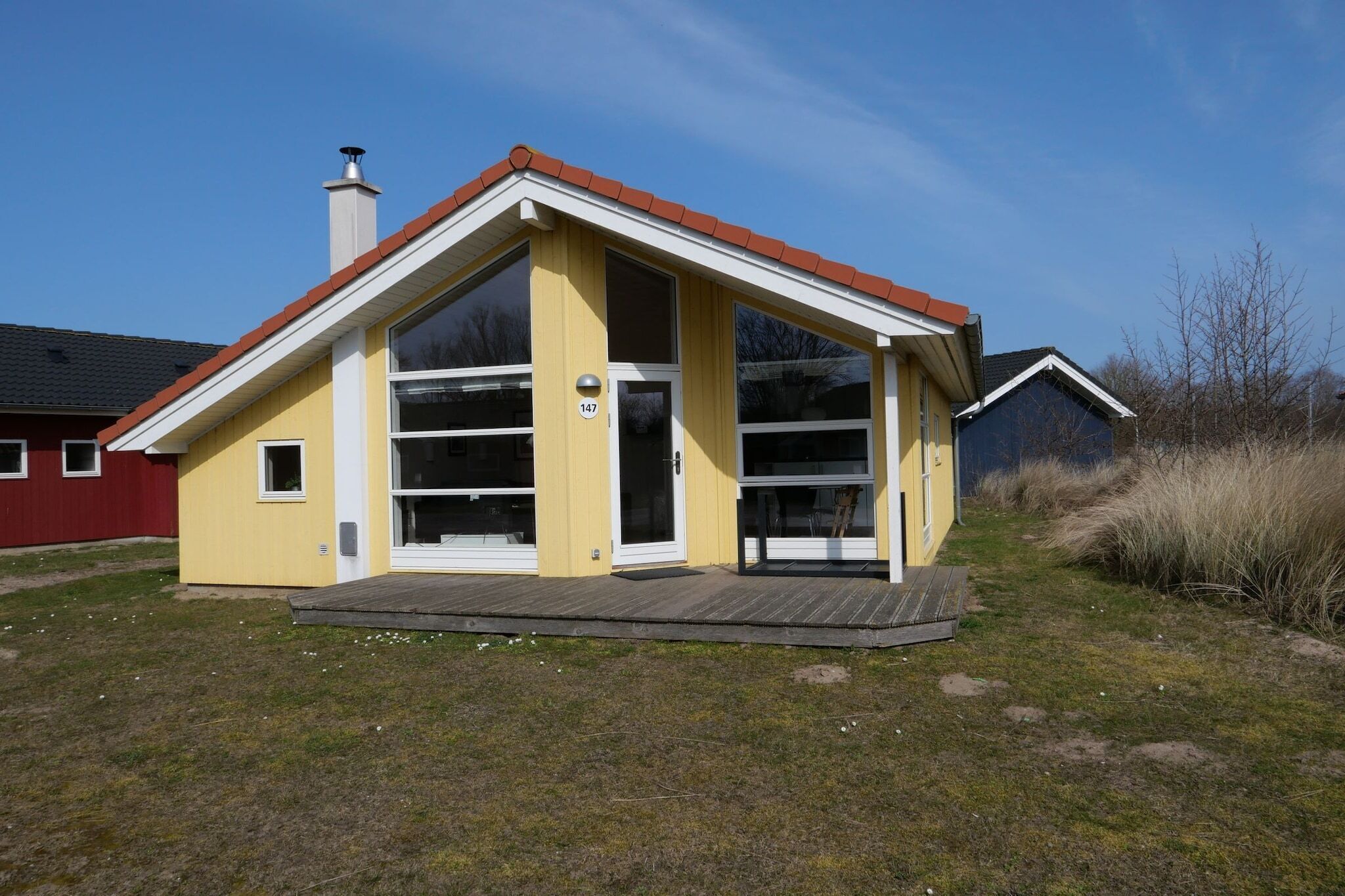 A yellow single-story house with a red roof, a chimney, and a large window.