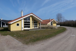 A yellow building with a red roof, a covered porch, and a gravel driveway. - Nordische Küstenflucht mit Sauna (Großenbrode)