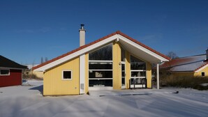 Un edificio amarillo con techo rojo, una chimenea y un ventanal grande.