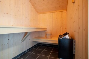A sauna with wooden walls, a tiled floor, a shelf, and a trash bin. - Resort Spa House für 8 Personen (Großenbrode)