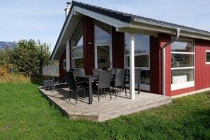 A red building with a covered patio area, outdoor seating, and a view of the surrounding landscape. - Resort Spa House für 8 Personen (Großenbrode)