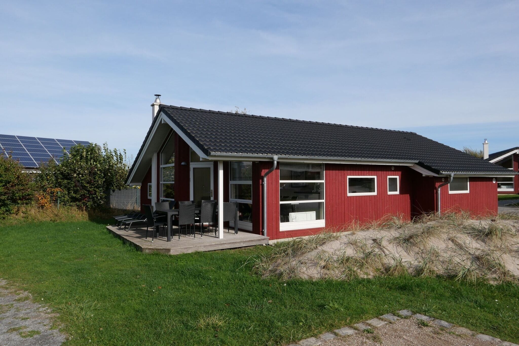 Un bâtiment rouge avec un toit en pente, un patio couvert avec des chaises, et un ensemble de panneaux solaires en arrière-plan.