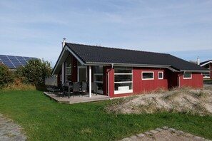 En röd byggnad med ett sluttande tak, en täckt uteplats med stolar och en solcellsanläggning i bakgrunden.