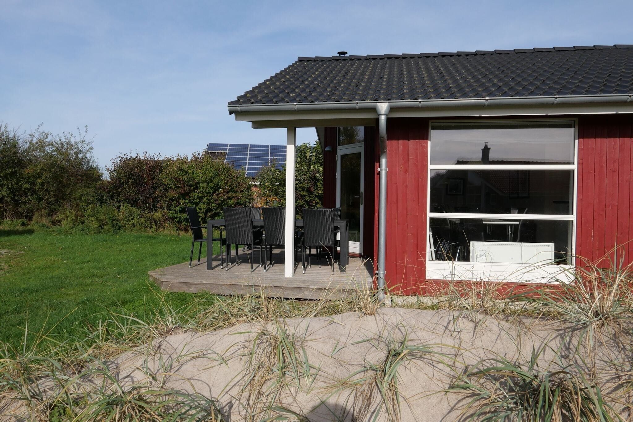 A red building with a covered patio area, outdoor seating, and a view of a solar panel installation in the background.
