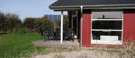 Un bâtiment rouge doté d’un patio couvert, d’un espace extérieur aménagé pour s’asseoir et offrant une vue sur une installation de panneaux solaires en arrière-plan.
