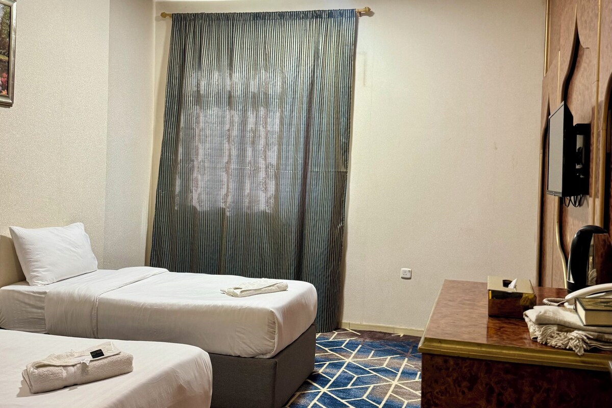 Habitación de hotel con dos camas, un escritorio y teléfono, y una alfombra estampada.