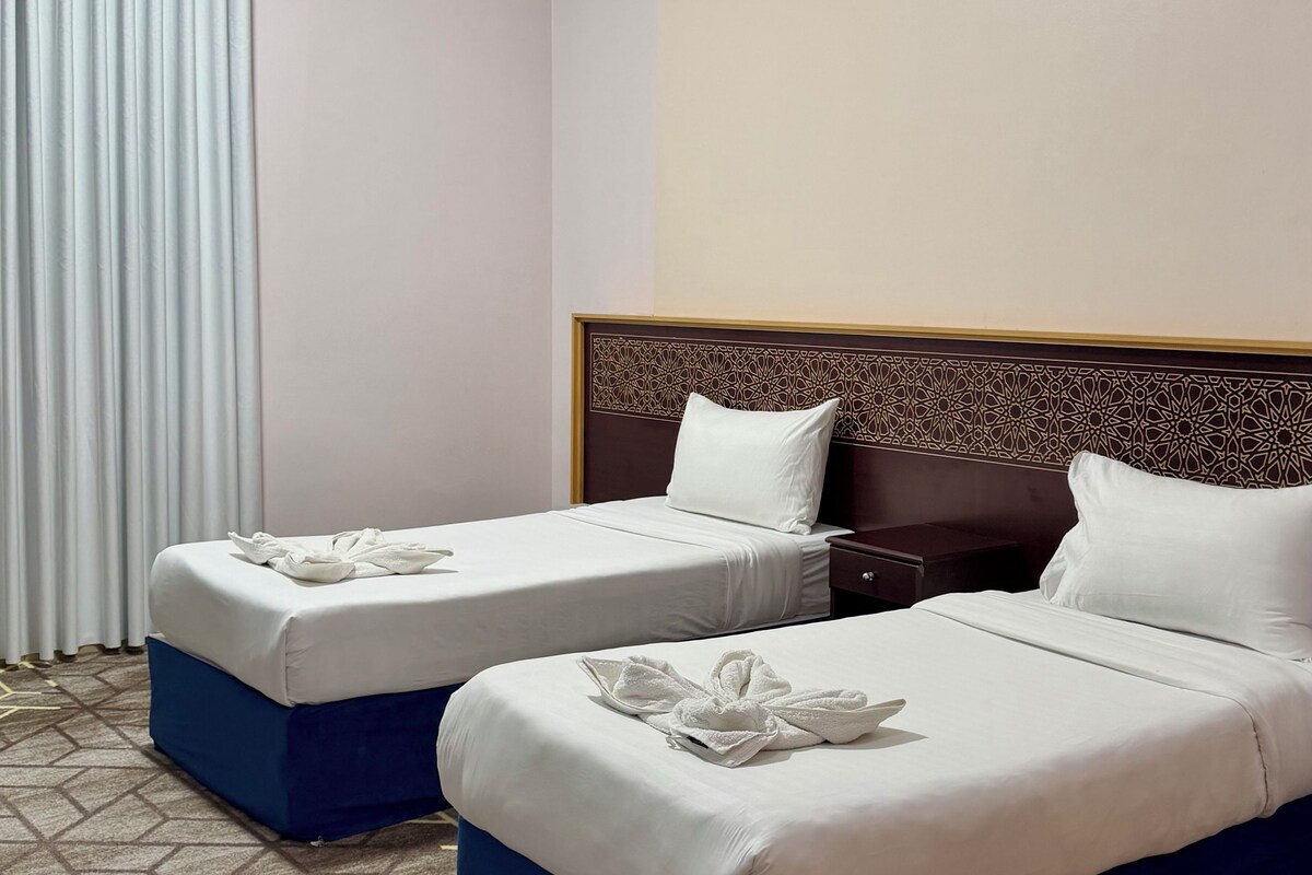Una habitación de hotel con dos camas, cabecero estampado y alfombra geométrica.
