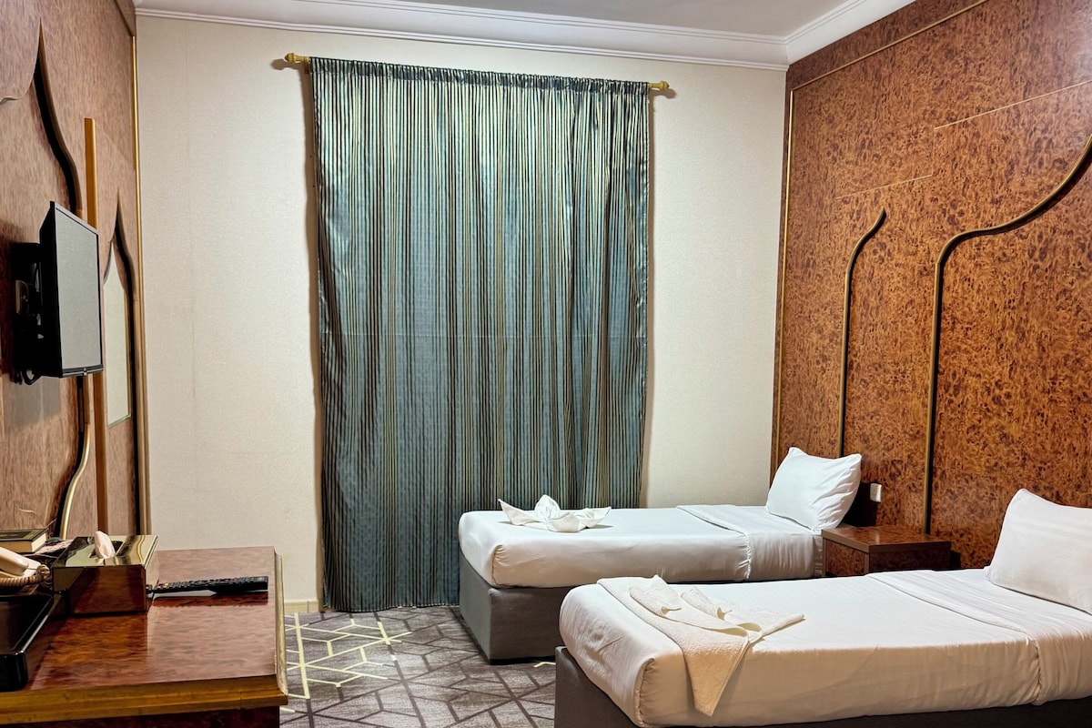 Habitación de hotel con dos camas, un escritorio, un teléfono y un televisor montado en la pared.