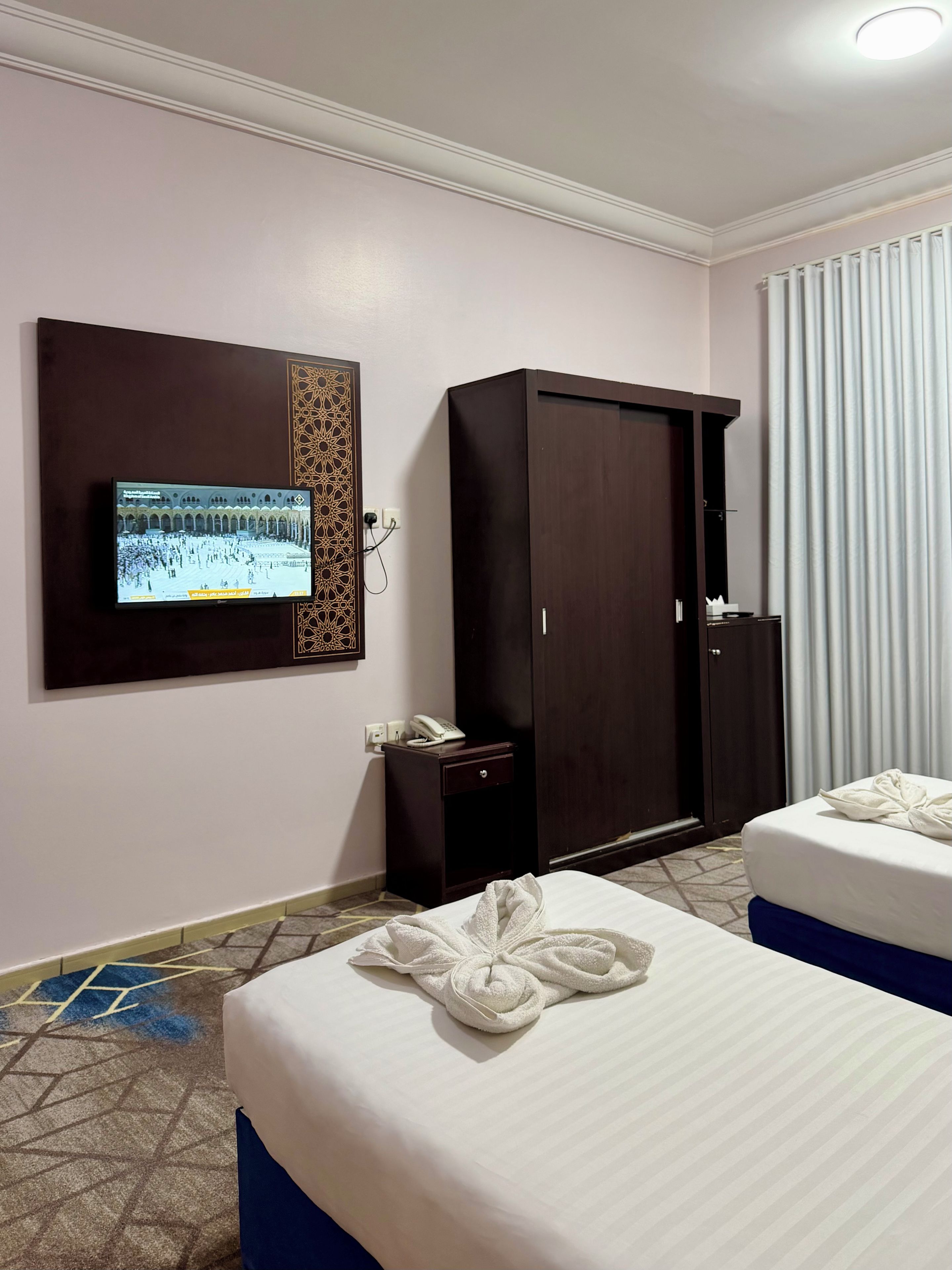 Habitación de hotel con cama, armario, mesita de noche con teléfono y televisión montada en la pared.
