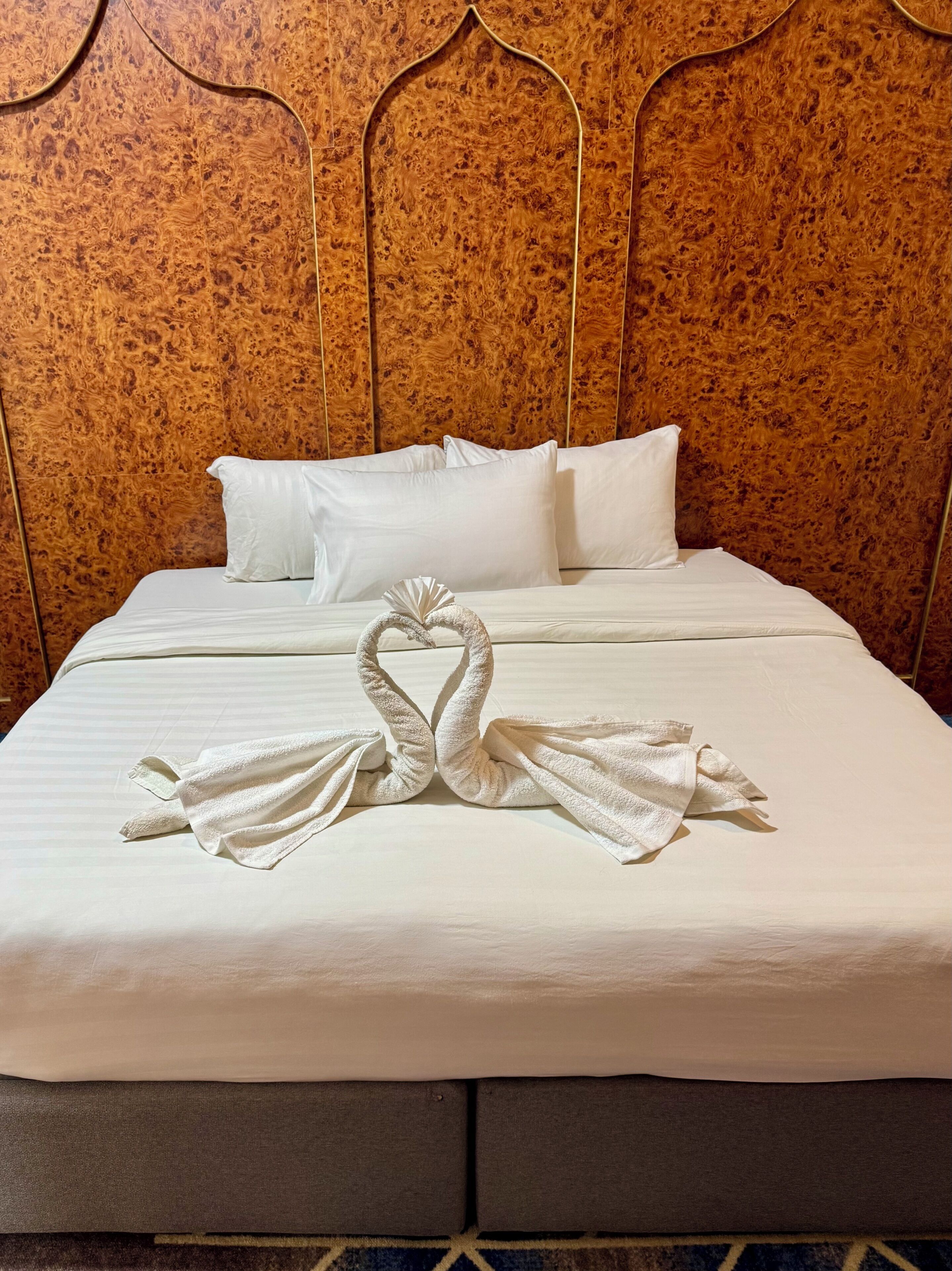 Habitación de hotel con una cama, ropa blanca y una escultura de toalla con forma de cisne.