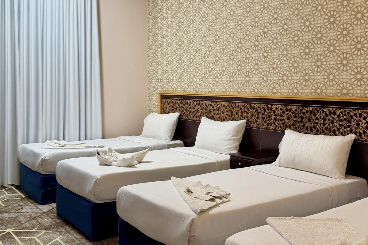 Una habitación de hotel con tres camas, un papel tapiz estampado y una alfombra geométrica.