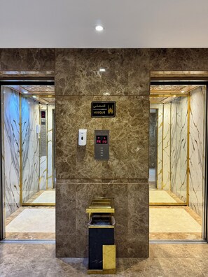 Interior de un ascensor con paredes de mármol, una pantalla digital y un cartel que indica que se encuentra en una mezquita.