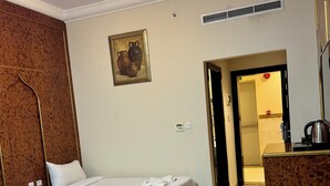 Habitación de hotel con dos camas, un armario de madera, un cuadro, un radiador y un baño visible a través de una puerta abierta.