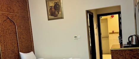 A hotel room with two beds, a wooden wardrobe, a painting, a radiator, and a bathroom visible through an open door.