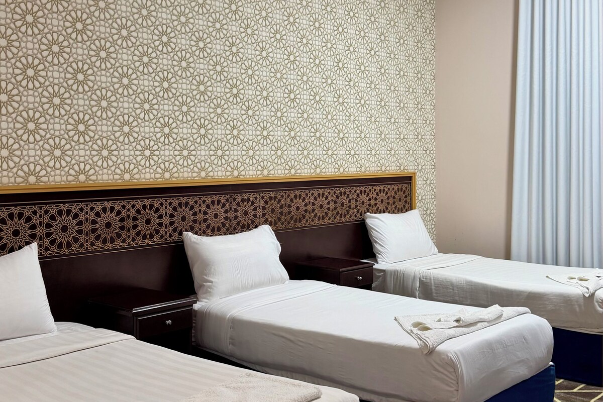 Habitación de hotel con tres camas, un papel tapiz estampado y una ventana con cortinas.