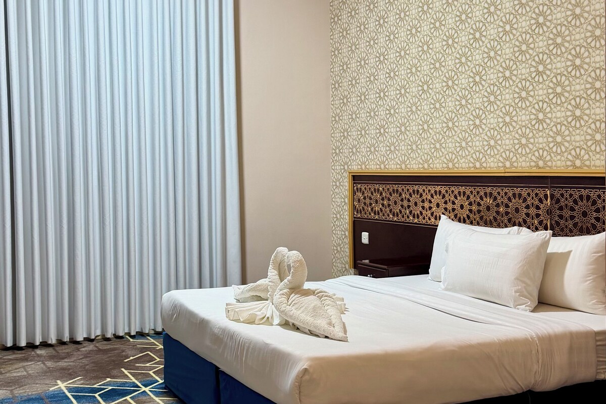 Habitación de hotel con cama, cortinas, pared estampada y alfombra geométrica.