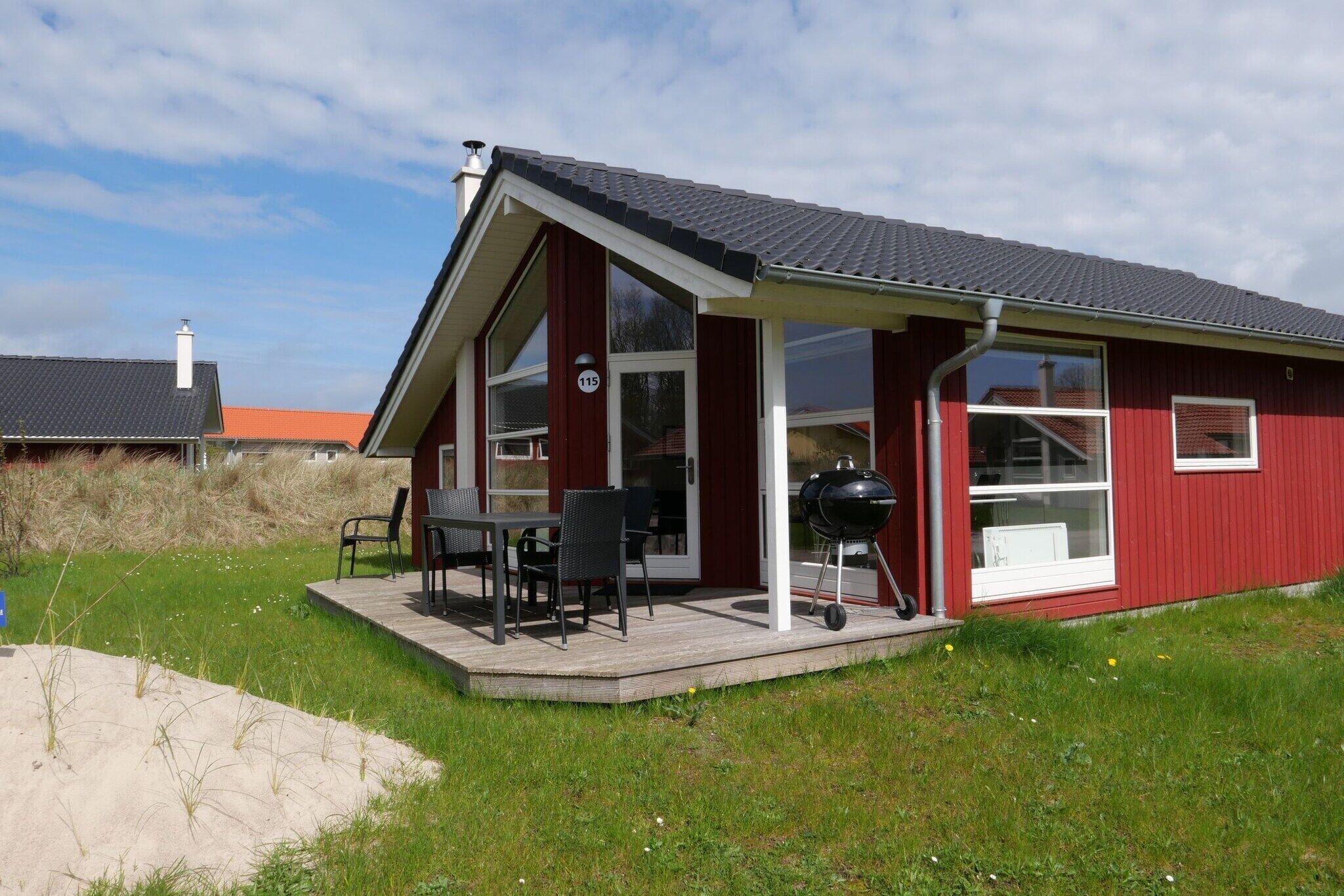 Ein rotes Gebäude mit einer überdachten Terrasse, einem Grill und einem Schild mit der Nummer 115.