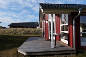 A modern building with a red exterior, a covered porch, and a clear sky. - Küstenfamilienchalet mit Sauna (Großenbrode)