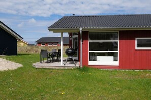 A red building with a covered patio, a grill, and a window. - Küstenfamilienchalet mit Sauna (Großenbrode)