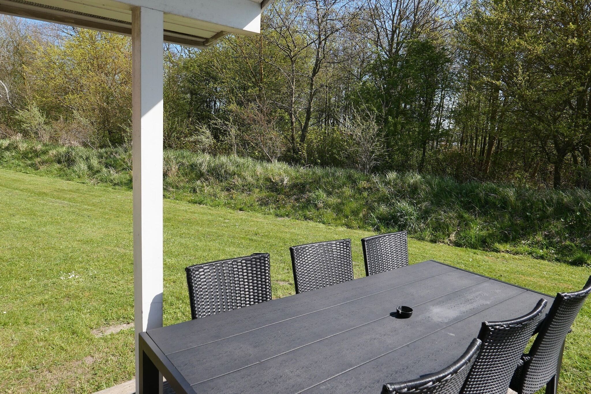 Un patio exterior con una mesa y sillas, rodeado de follaje y árboles.