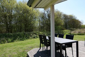 Eine Terrasse im Freien mit Tisch und Stühlen, umgeben von Rasen und Bäumen.
