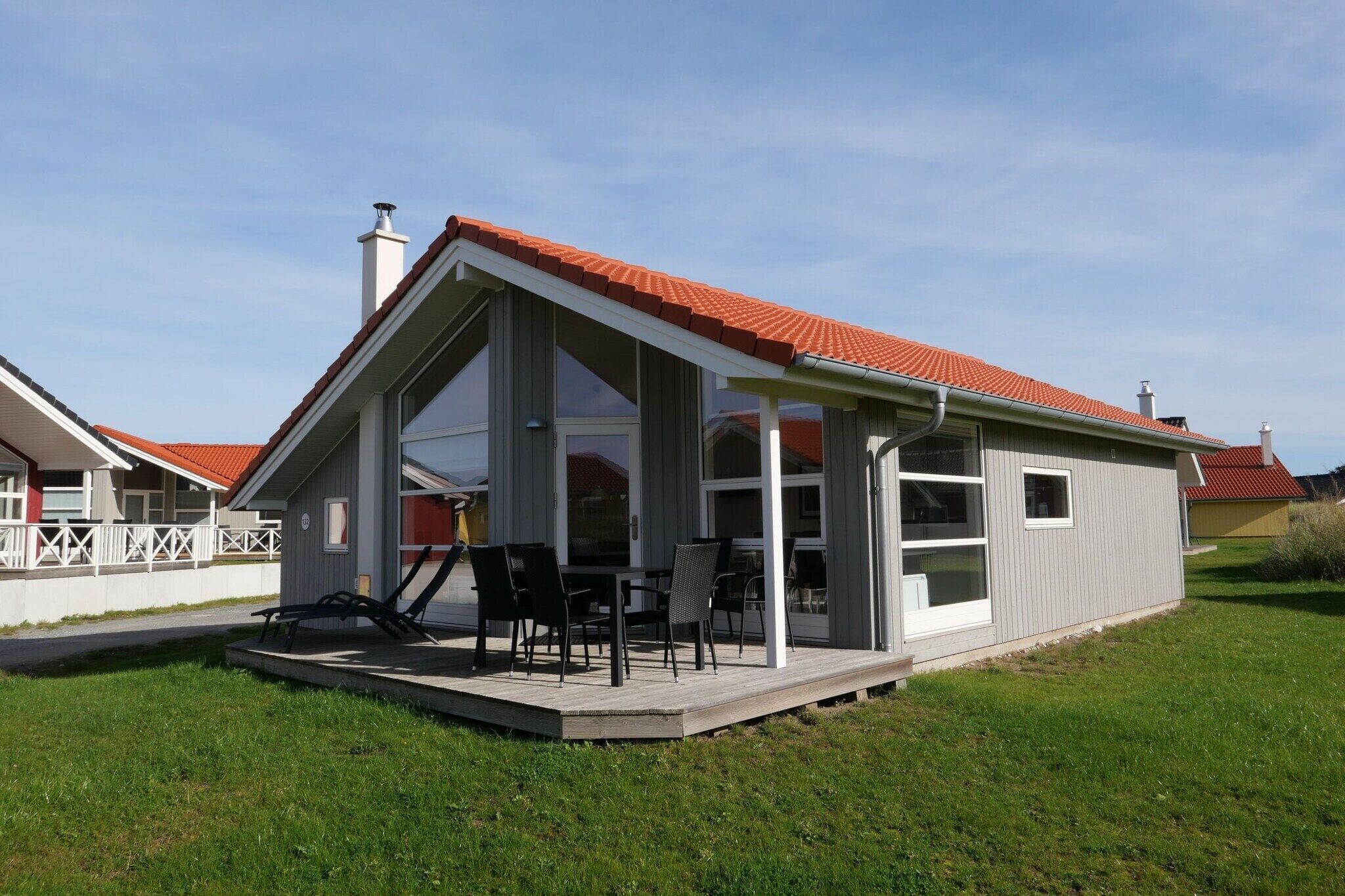 Une maison moderne dotée d’un patio couvert, de grandes fenêtres et d’un toit recouvert de tuiles rouges.