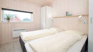 Un dormitorio con dos camas, una ventana con vistas, un radiador y una estantería con libros.