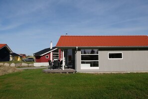 A single-story building with a red-tiled roof, a covered patio area with outdoor furniture, and a large window on the side. - Familienversteck für 6 in Großenbrode (Großenbrode)