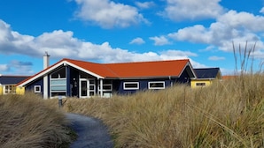 A coastal building with a red roof, large windows, and a pathway leading to it. - Chalet im skandinavischen Stil für 6 Personen (Großenbrode)