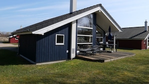 A modern house with a sloped roof, a chimney, and a covered patio area with outdoor furniture. - Chalet im skandinavischen Stil für 6 Personen (Großenbrode)