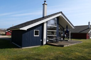 Ein modernes Haus mit geneigtem Dach, einem Schornstein und einer überdachten Terrasse mit Gartenmöbeln.