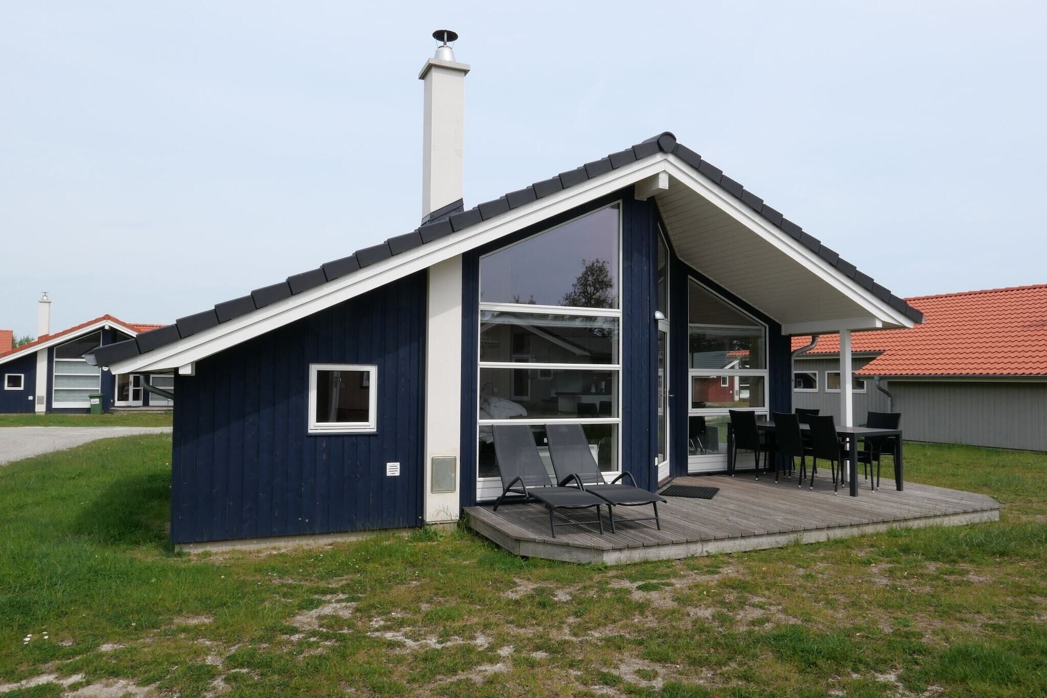 Ett modernt hus med en stor glasdörr, en liten terrass med utemöbler och en skorsten.