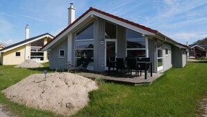 Uma casa térrea com telhado vermelho, janelas amplas e um pátio com mobiliário de exterior.