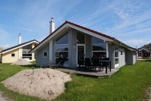 Einbungalow mit rotem Dach, großen Fenstern und einer Terrasse mit Gartenmöbeln.