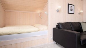 Um quarto pequeno com painéis de madeira, uma cama, um sofá de couro preto e duas luzes fixadas na parede.