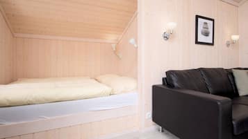 Ein kleiner Raum mit Holzwänden, einem Bett, einer schwarzen Ledersofa und zwei Wandleuchten.