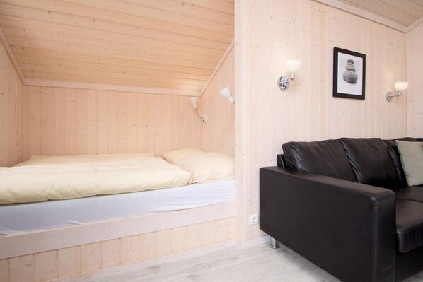 Ein kleiner Raum mit Holzwänden, einem Bett, einer schwarzen Ledersofa und zwei Wandleuchten.