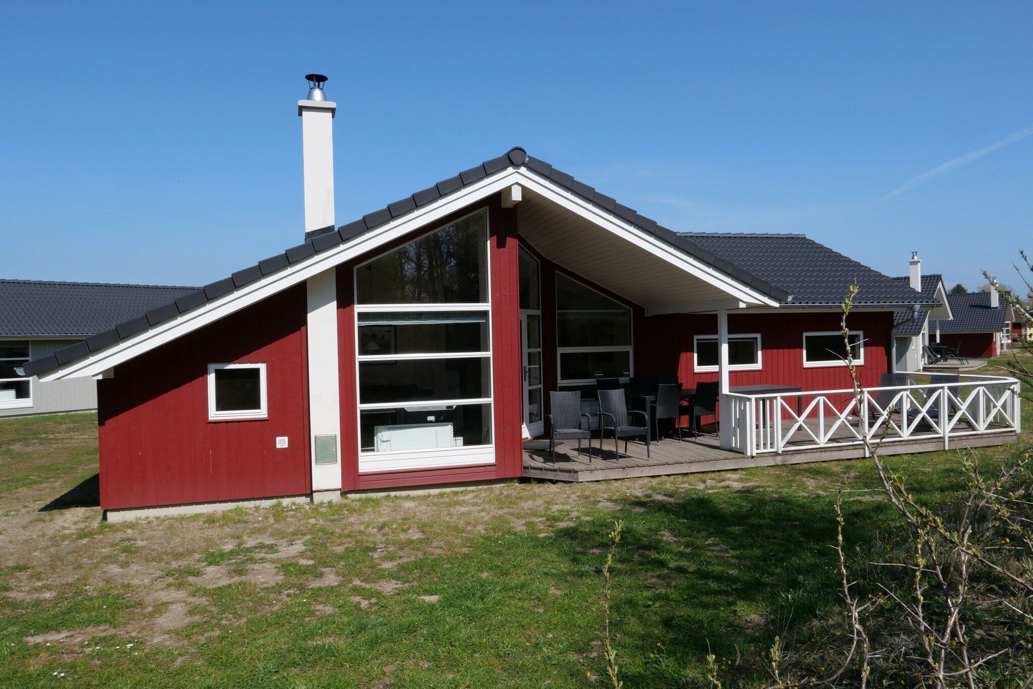 Un bâtiment rouge avec une grande fenêtre, une cheminée et une terrasse avec des chaises.