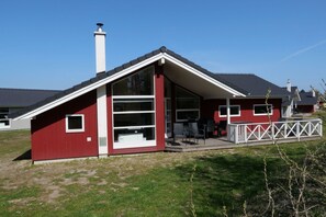 Ein rotes Gebäude mit einem großen Fenster, einem Schornstein und einer Terrasse mit Stühlen.